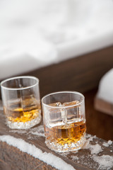 Two whiskey glasses in the snow on a winter background.