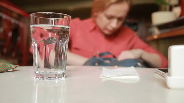 girl in cafe is looking for something in a bag on a glass background with water