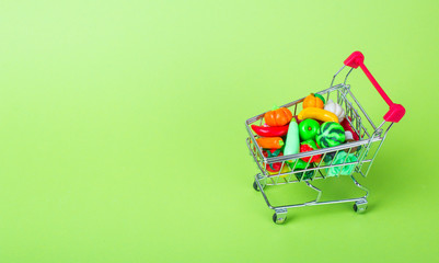 Metal shopping cart with fruits and vegetables on a green background