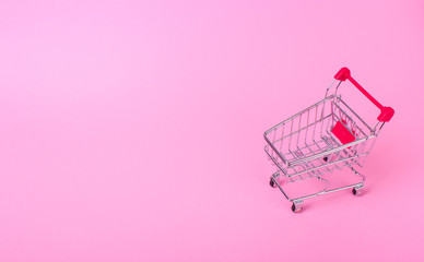 Empty shopping cart with the red handle on a pink background