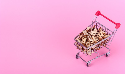 Shopping basket with letters of the alphabet made of wood on a pink background