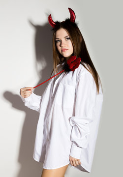 young girl in a man's white shirt with red horns holding trident and looks like pretty Devil