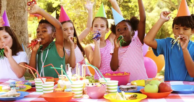 Group of kids blowing party horn while celebrating a birthday in park 4k