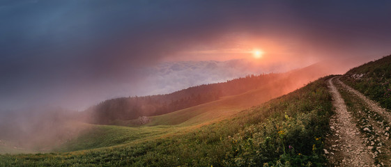 Dirt road in the mountains with panoramic view of great sunset with fog or cloud