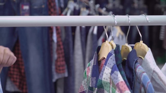 closeup details persone hand choose shirt in the shop. rack with clothes hanger different colored casual shirts.