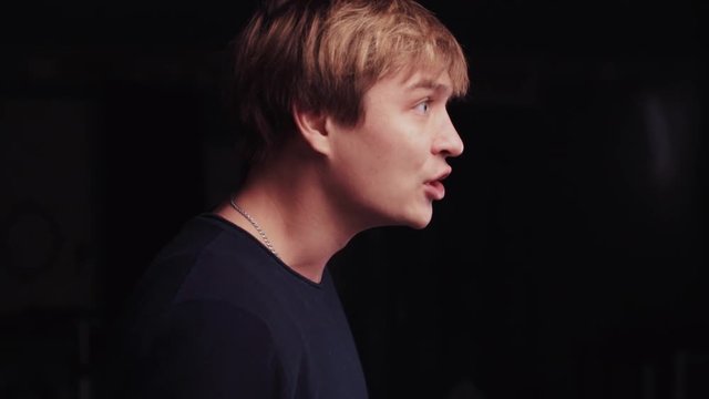 Close up view of stylish blonde man in a classical black sweater. Aggressive man is arguing with somebody actively gesticulating and not looking forward to the camera. Conflict situation.