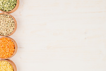 Assortment of lentils in a wooden bowls with copy space on white wood background. Top view, closeup. Healthy protein food.