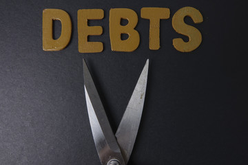 Scissors and word of DEBTS on black background. Business concept