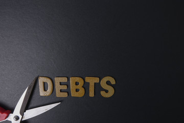 Scissors and word of DEBTS on black background. Business concept