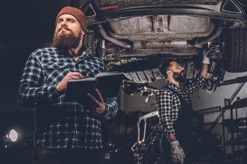 Obraz na płótnie Canvas Bearded mechanics male inspecting car.