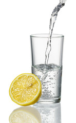 Glass of water with splashed lemon isolated on white