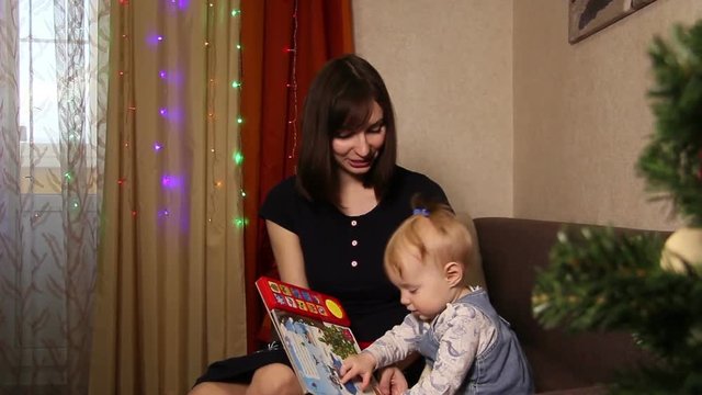 A young mother reads a children's book for a child.Children in the house.Christmas in the house.