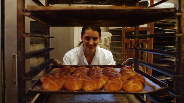 Female baker putting baked michetta in baking trolley at bakery kitchen 4k