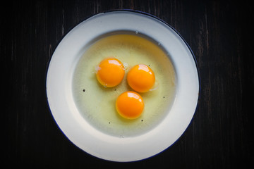 Three raw eggs in white metal plate on a black background