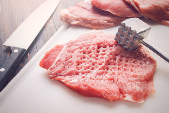Tenderized piece of raw meat on a white cutting board, with knife and tenderizer - Powered by Adobe