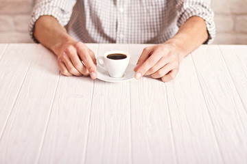 Coffee break. Man sitting on the white table with cup of espresso in the checked shirt. White bricks wall background