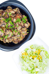 Fried mushrooms and green onion on a black plate and vegetable salad on a white plate