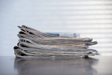 Stack of newspapers on a wooden surface. Curtain shadows in the background.