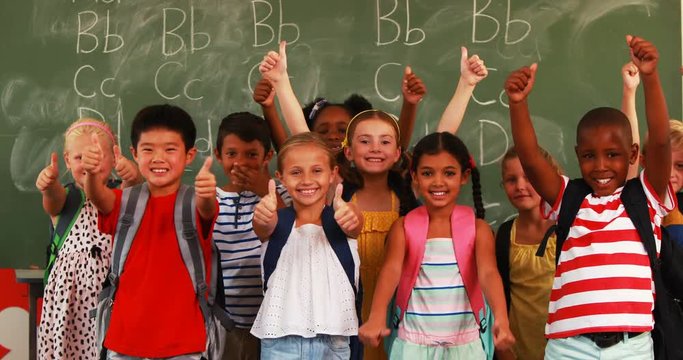 Portrait of smiling kids showing thumbs up in classroom at school 4k