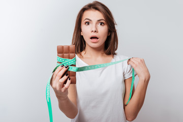 Confused young lady holding centimeter and chocolate