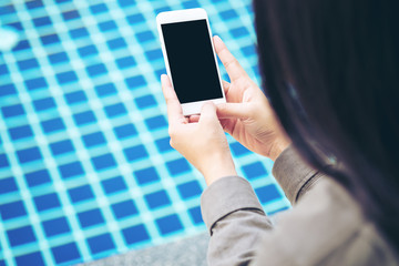 Mockup image of a woman showing smart phone with blank black screen by swimming pool