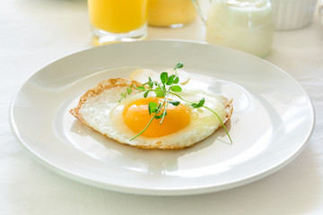 Traditional breakfast with fried egg, yogurt, homemade muffins, citrus curd and orange juice on white background. Selective focus. High key
