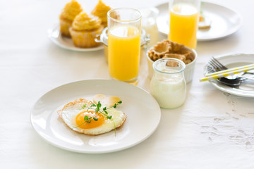 Traditional breakfast with fried egg, yogurt, homemade muffins, citrus curd and orange juice on white background. Selective focus. High key