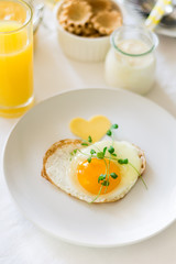 Traditional breakfast with fried egg, yogurt, homemade muffins, citrus curd and orange juice on white background. Selective focus. High key