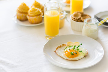 Traditional breakfast with fried egg, yogurt, homemade muffins, citrus curd and orange juice on white background. Selective focus. High key