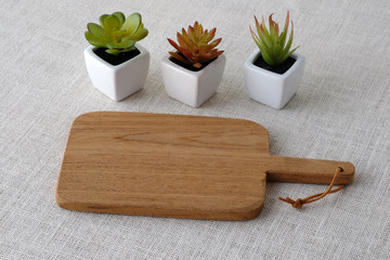 Empty wooden chopping board and small tree pots on sack tablecloth, food display montage background
