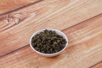 dried chinese tea leaves in a small bowl over wooden background
