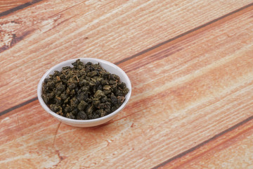 dried chinese tea leaves in a small bowl over wooden background