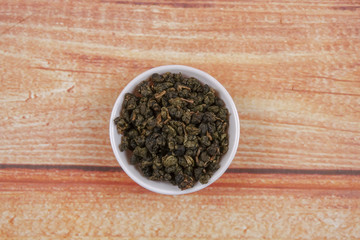 dried chinese tea leaves in a small bowl over wooden background