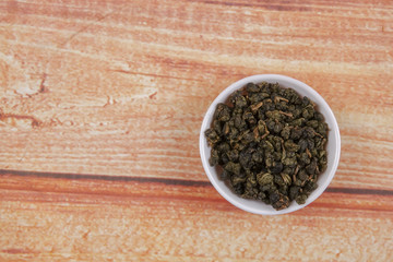 dried chinese tea leaves in a small bowl over wooden background