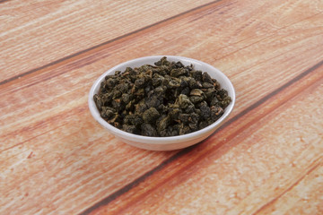 dried chinese tea leaves in a small bowl over wooden background