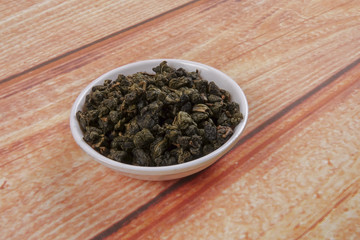 dried chinese tea leaves in a small bowl over wooden background