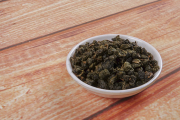 dried chinese tea leaves in a small bowl over wooden background