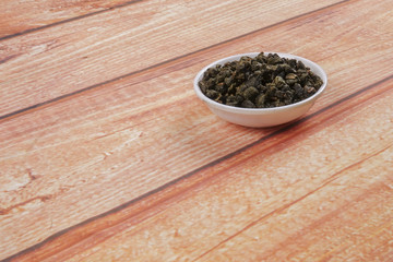 dried chinese tea leaves in a small bowl over wooden background