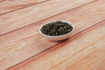 dried chinese tea leaves in a small bowl over wooden background