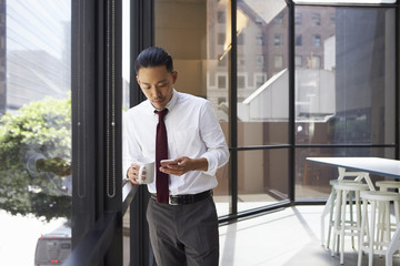 Asian businessman standing in modern office using phone