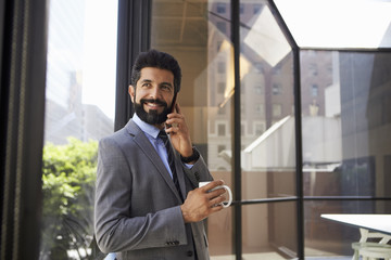 Middle aged Hispanic businessman using phone and holding cup