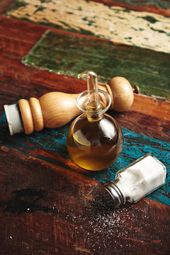 Wooden pepper grinder and sea salt in vintage jar lying on aged wooden sorface of table or floor next to small transparent dispencer with virgin extra olive oil inside, vertical shot