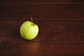 Sweet small green apple isolated on left side on aged wooden table, close up