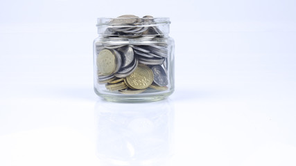 Glass jar with coins on white background