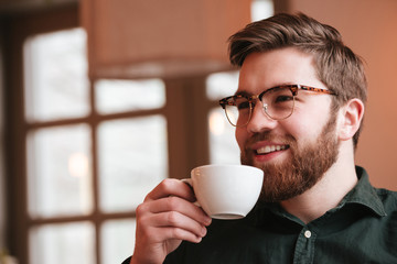 Happy bearded young man drinking coffee.