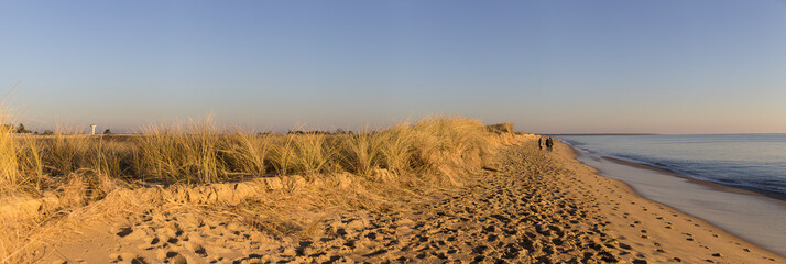 panoramic picture with people walking on the beach by romantic winter sunset