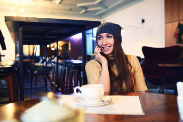 Portrait of beautiful girl in hat using her mobile phone in cafe. Tonned. Selective focus.
