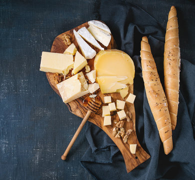 Cheese plate. Assortment of cheese with walnuts, honey and bread on olive wood serving board with textile over dark blue canvas as background. Top view with space.