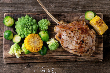 Grilled veal tomahawk steak with vegetables brussels sprouts, romanesco and corn cobs served on...