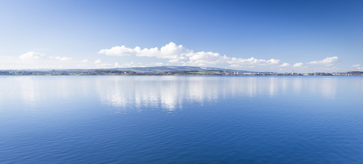 Obraz premium Clear day. Lake Zug in central Switzerland. Clouds are reflected in water lake. At the edge water is clear and see the bottom of the lake.